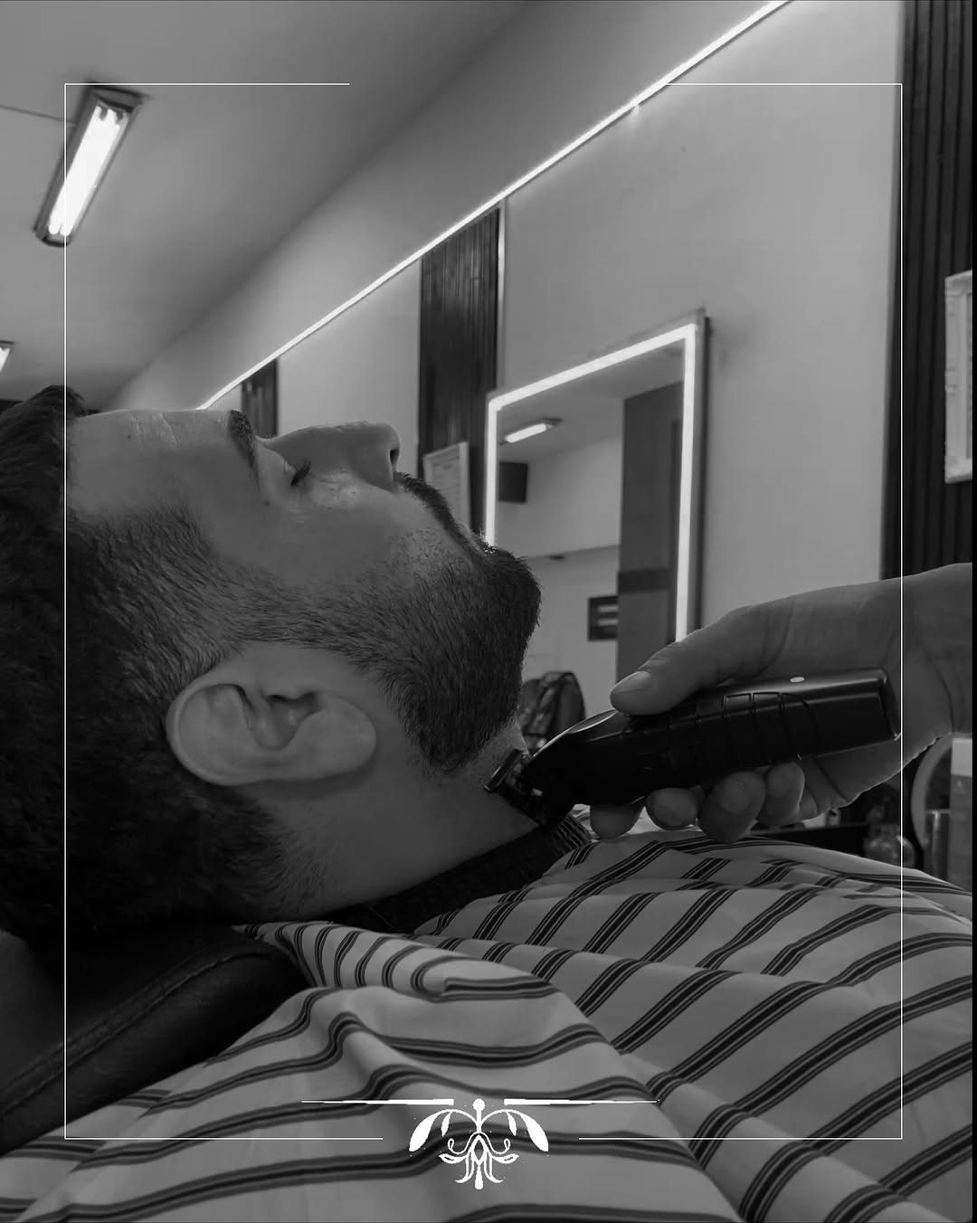 Barbero perfilando la barba de un cliente con máquina en la barbería